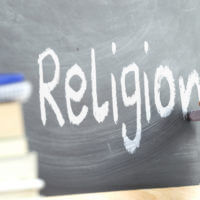 A person writing "religion" on a blackboard